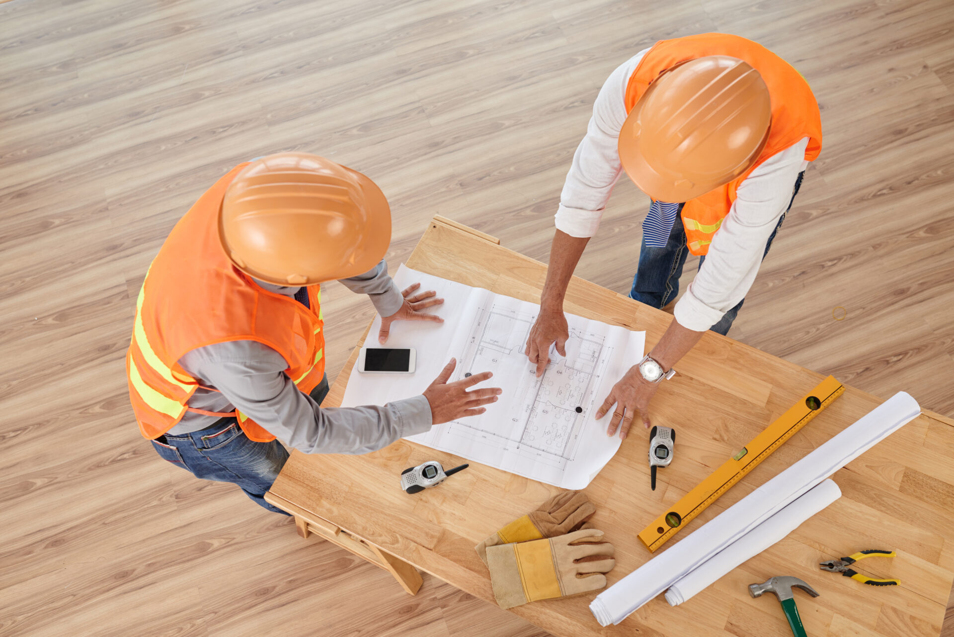 Engineers in hard hats discussing blueprint of the building on table, view from above